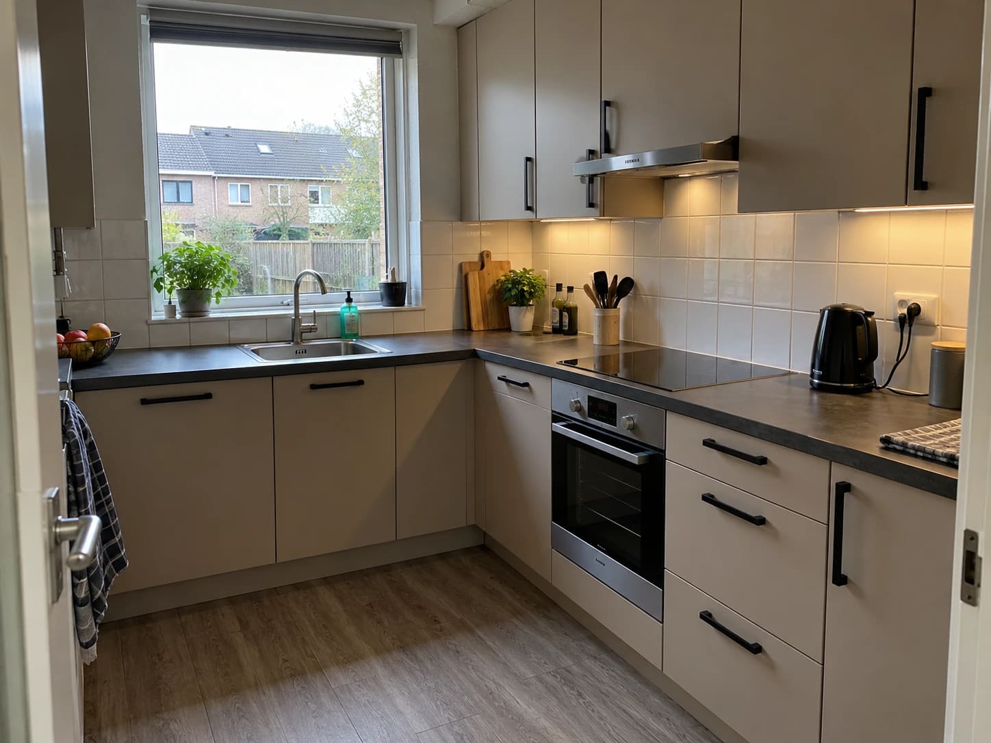 Gewrapte keuken met matte beige keukenkastjes, zwarte grepen en een donker werkblad
